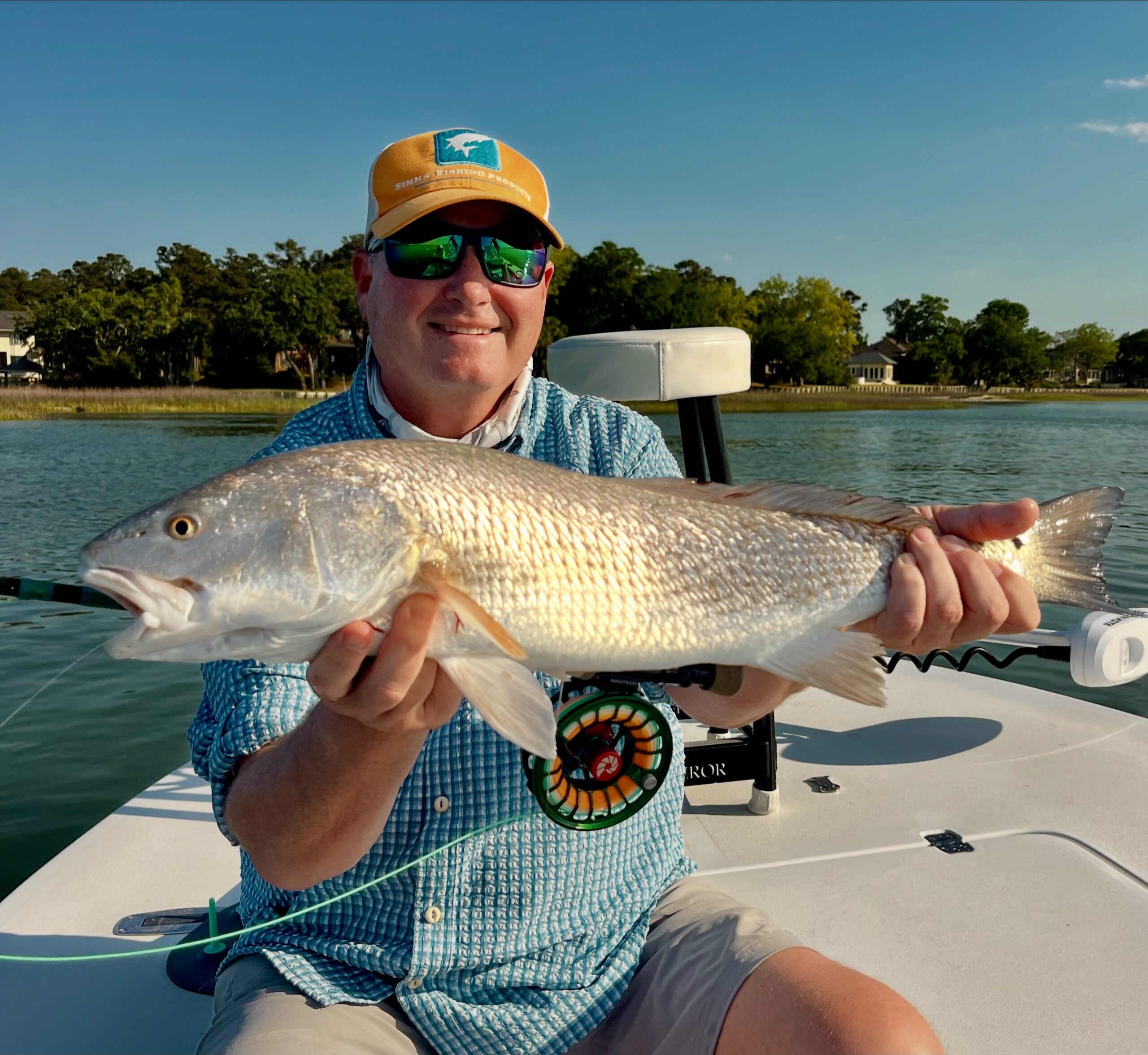 Eley Duke III in a cap and sunglasses holding a red drum on a boat, with a fly rod and reel in his lap