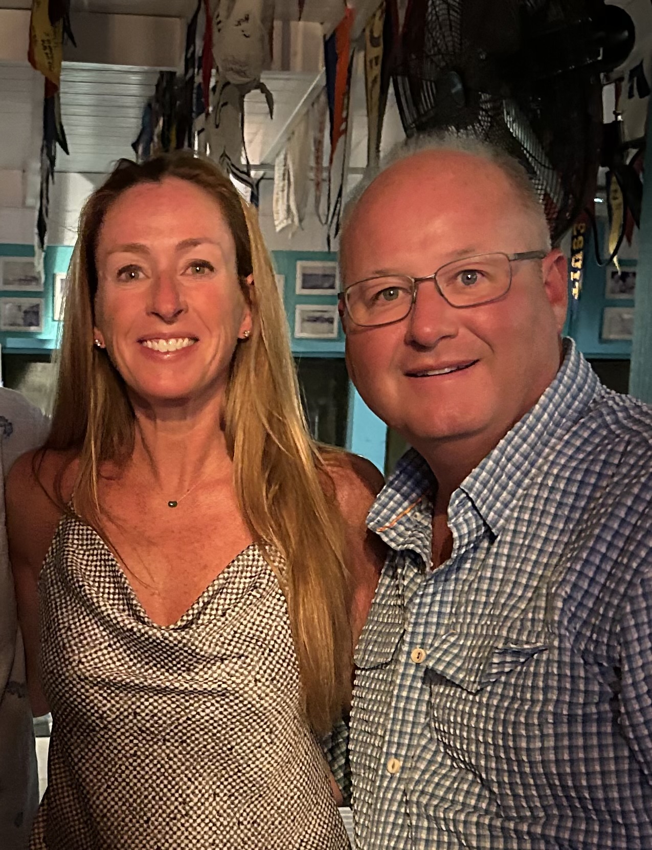 Eley Duke III and his wife, Nicole Harrell, smiling together indoors beneath hanging pennants