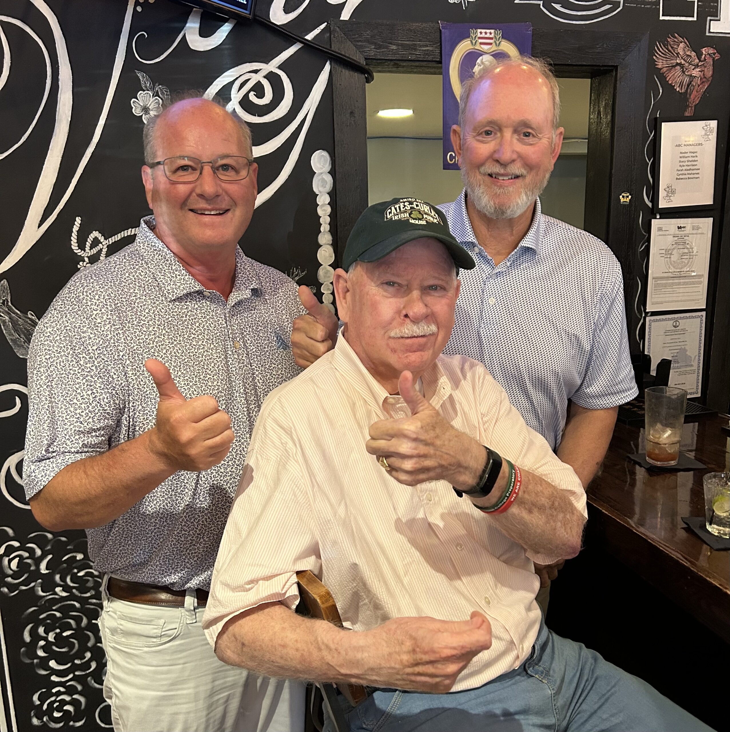 Eley Duke III, Johnny Cates and Don Hall giving a thumbs-up inside a restaurant with a hand-painted chalkboard wall