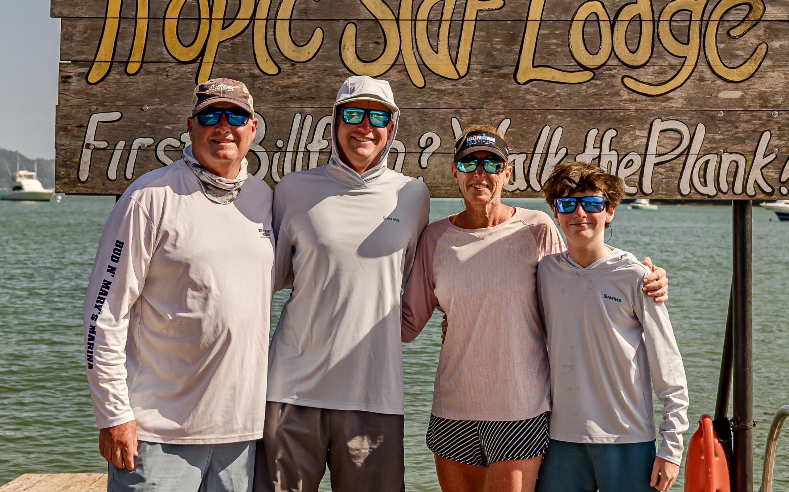 Eley Duke III, Parker, Nicole Harrell and E standing on a dock in front of the Tropic Star Lodge sign